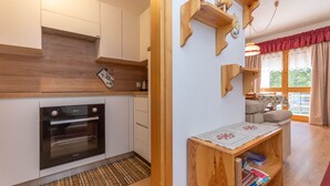 A modern kitchen with white cabinets, a built-in oven, and wooden shelves. - Appartamento Cordevole (Rocca Pietore)