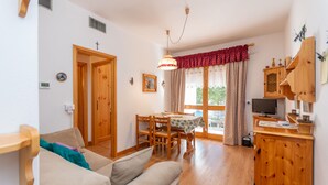 A cozy living room with a sofa, wooden dining table, and a TV stand. - Appartamento Cordevole (Rocca Pietore)