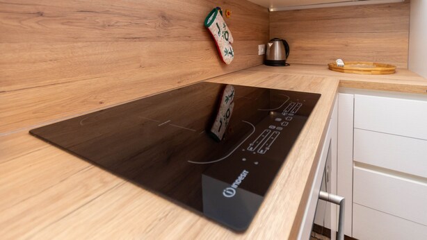 A modern kitchen with a black induction cooktop, wooden cabinetry, and a stainless steel kettle. - Appartamento Cordevole (Rocca Pietore)