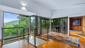Amplia habitación con grandes puertas correderas de vidrio que dan a una terraza con vistas a exuberante follaje.