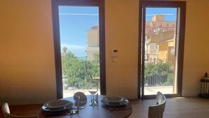 Un'area pranzo con tavolo apparecchiato per due persone, due sedie e vista su un balcone con ringhiera e vegetazione.