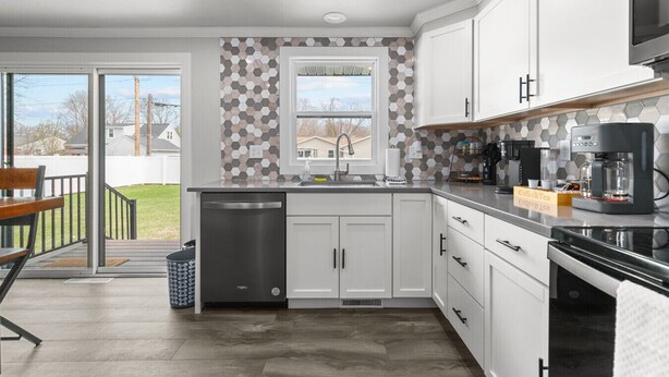 A modern kitchen with white cabinets, a stainless steel dishwasher, a coffee station, and a view of the outdoors. - LAMBEAUView|7 MinWalk|Sleeps10 (Green Bay)