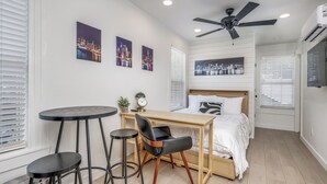 Ein Schlafzimmer mit einem Bett, einem Schreibtisch, zwei Stühlen, einem Deckenventilator und Stadtbildern an den Wänden.