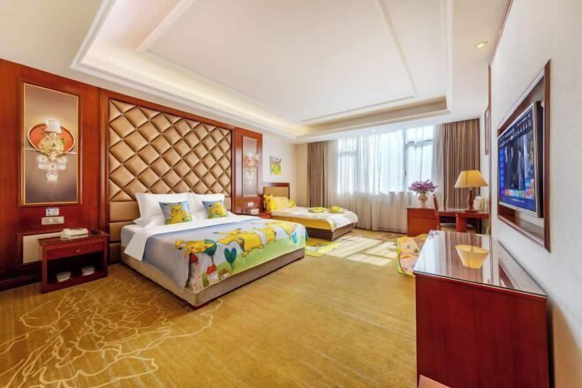 A hotel room with a large bed, a smaller bed, a desk, and a TV.