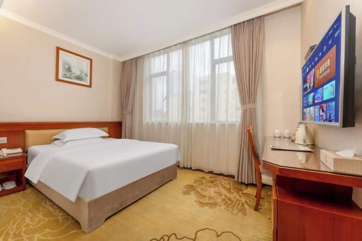 A hotel room with a bed, a desk, a television, and a window with curtains.
