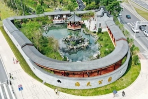 Um pavilhão tradicional com telhado curvo, um lago central e uma passarela ao redor.