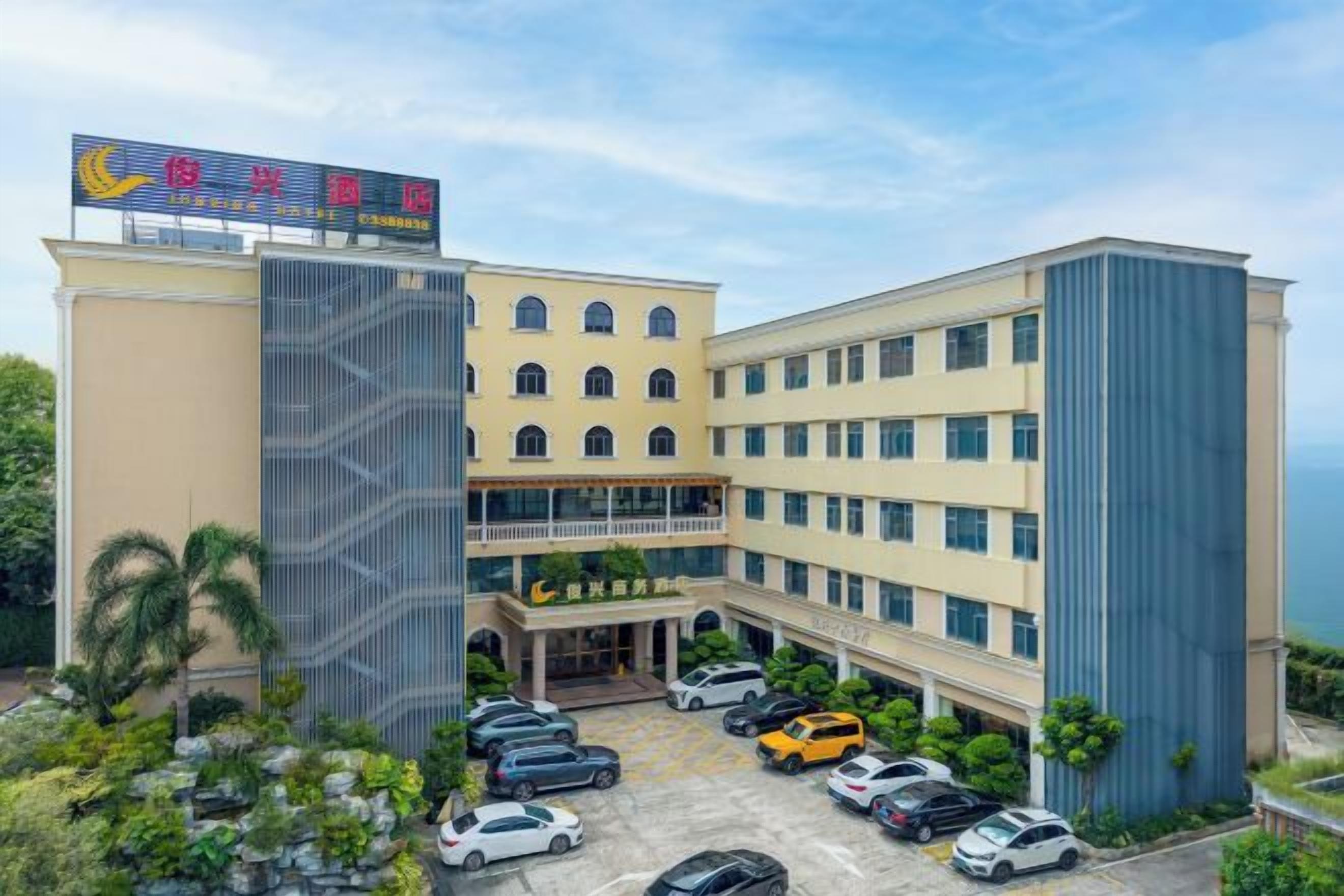 A multi-story hotel with a central courtyard, a parking area, and a view of the sea.