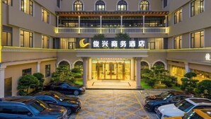 A hotel with a central entrance, multiple floors, and a parking area with cars. - Junxing Business Hotel (Lovers' Road Youtehui Shopping mall) (Zhuhai)