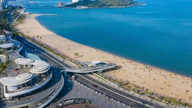 Un paisaje urbano costero con una playa, arquitectura moderna y una carretera que conduce a un edificio con cúpula blanca.