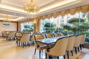 A dining area with tables and chairs, large windows, and a chandelier.