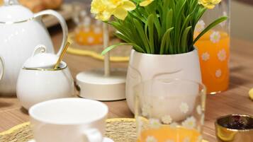 A table set with white teapots, cups, a vase with yellow flowers, and a glass with orange juice.