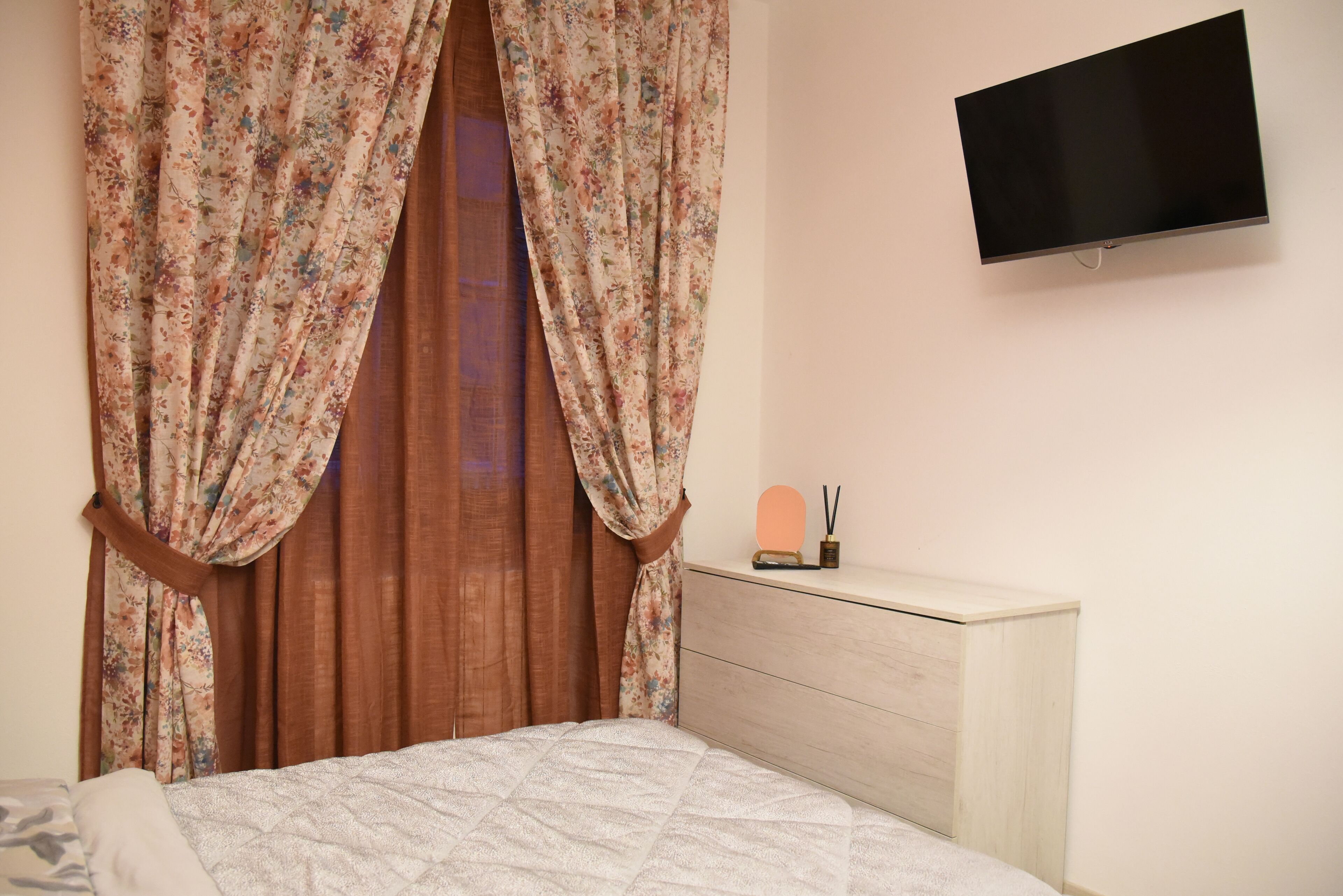 Une chambre à coucher avec un lit, une commode, un téléviseur à écran plat et des rideaux à motifs floraux.