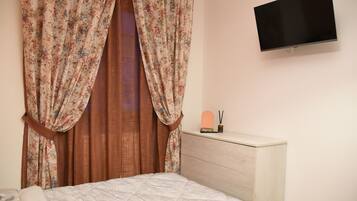 Une chambre à coucher avec un lit, une commode, un téléviseur à écran plat et des rideaux à motifs floraux.