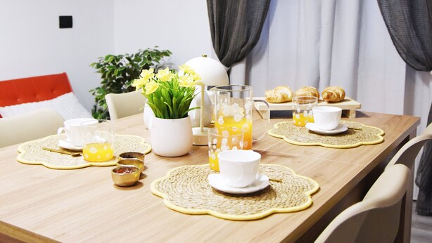Una mesa de comedor dispuesta con un reloj, flores y comida para el desayuno.