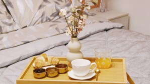 Una bandeja con croissants, mermelada, una taza y un vaso de jugo de naranja sobre una cama con un florero.