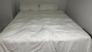 Ein kleines Zimmer mit einem Einzelbett, weißer Bettwäsche und schlichten Wänden.