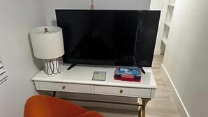 Ein Zimmer mit einem weißen Schreibtisch, einem schwarzen Flachbildfernseher, einer Lampe und einem roten Sessel.