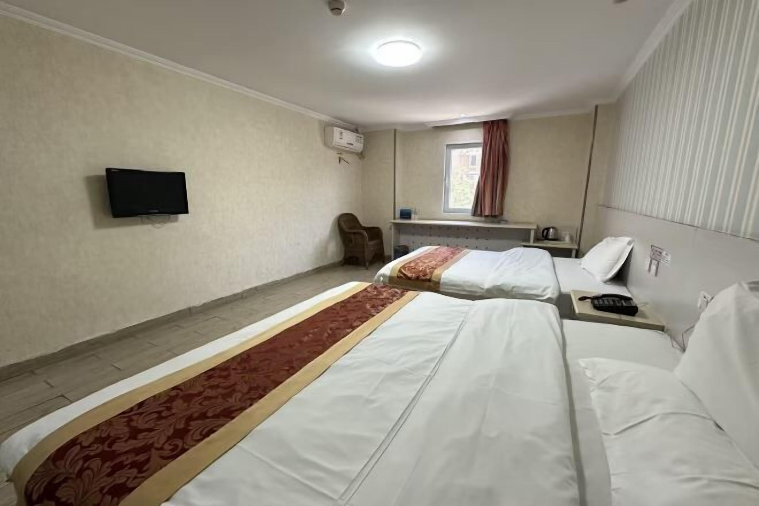 Habitación de hotel con dos camas, televisión, ventana con cortinas, una silla y una mesita.