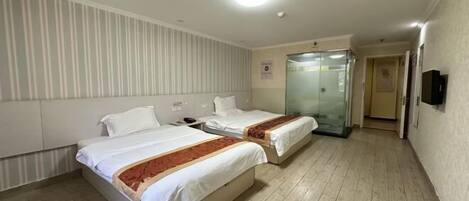 Une chambre d’hôtel avec deux lits, une salle de bain avec une porte en verre et un téléviseur fixé au mur.