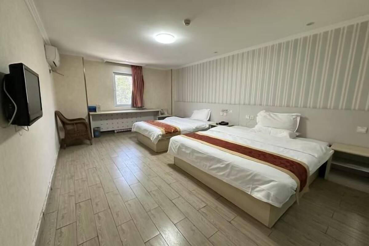 A hotel room with two beds, a television, a window with curtains, and a striped wall.