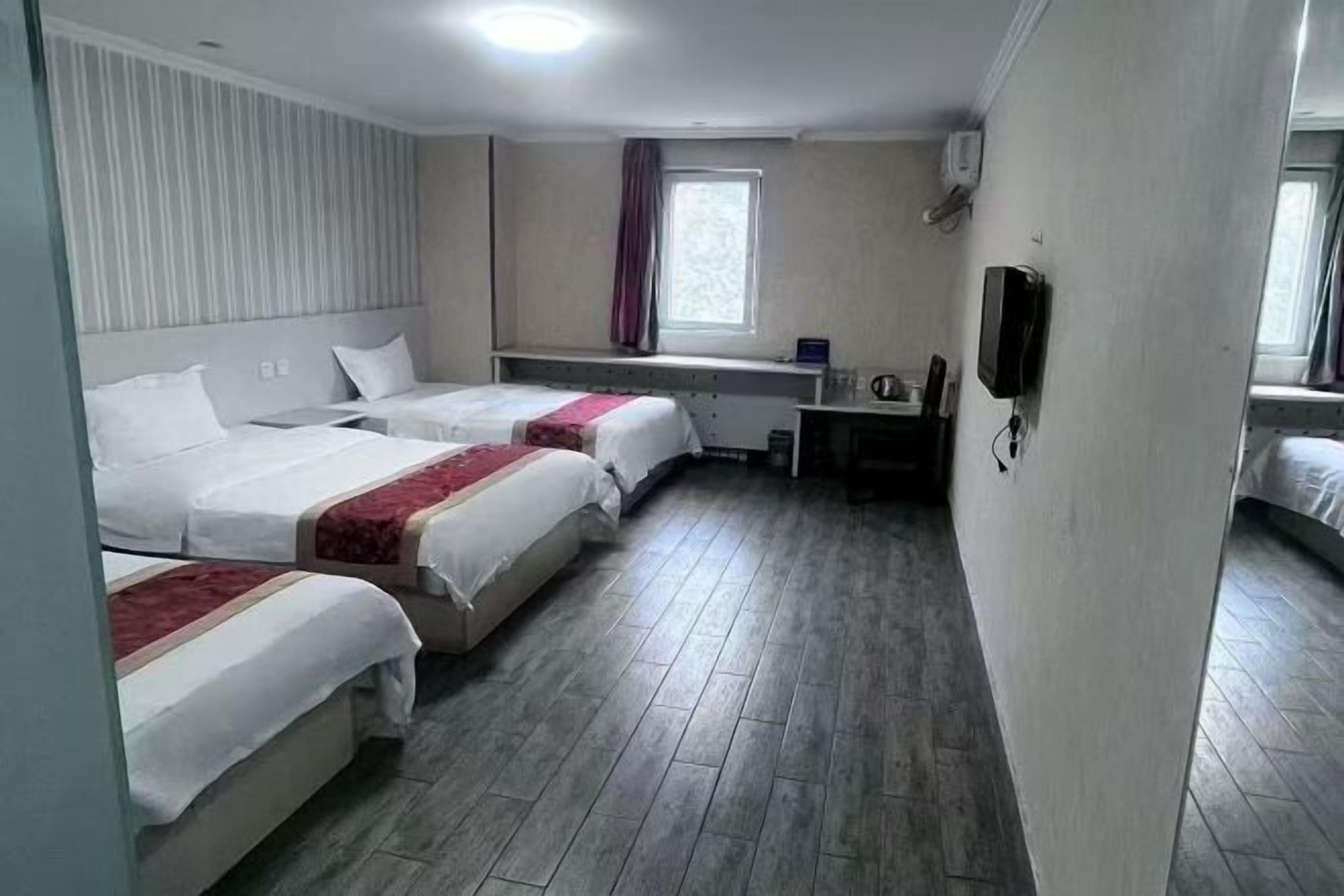 A hotel room with three beds, a desk, a chair, a television, and a window with curtains.