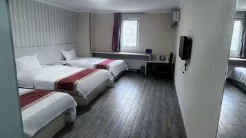 A hotel room with three beds, a desk, a chair, a television, and a window with curtains.