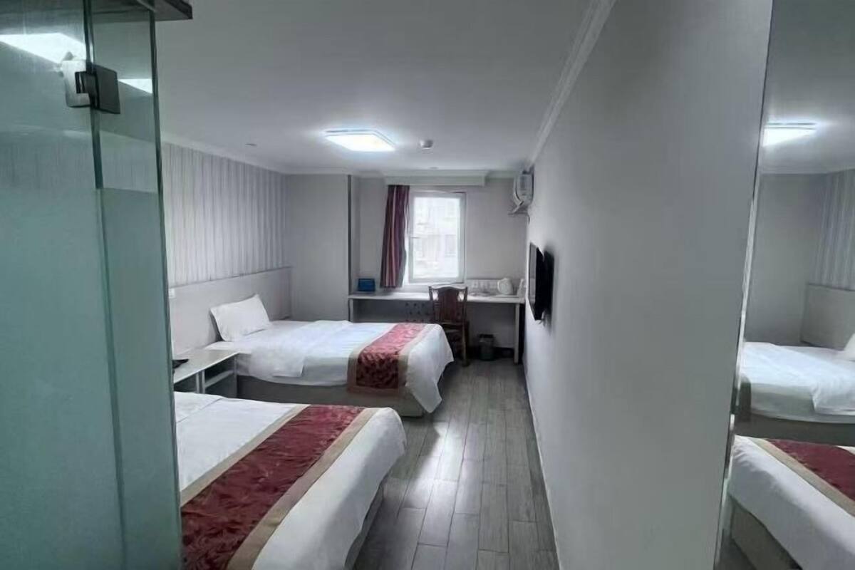 A hotel room with two beds, a desk, a chair, a window with curtains, and a mirror.