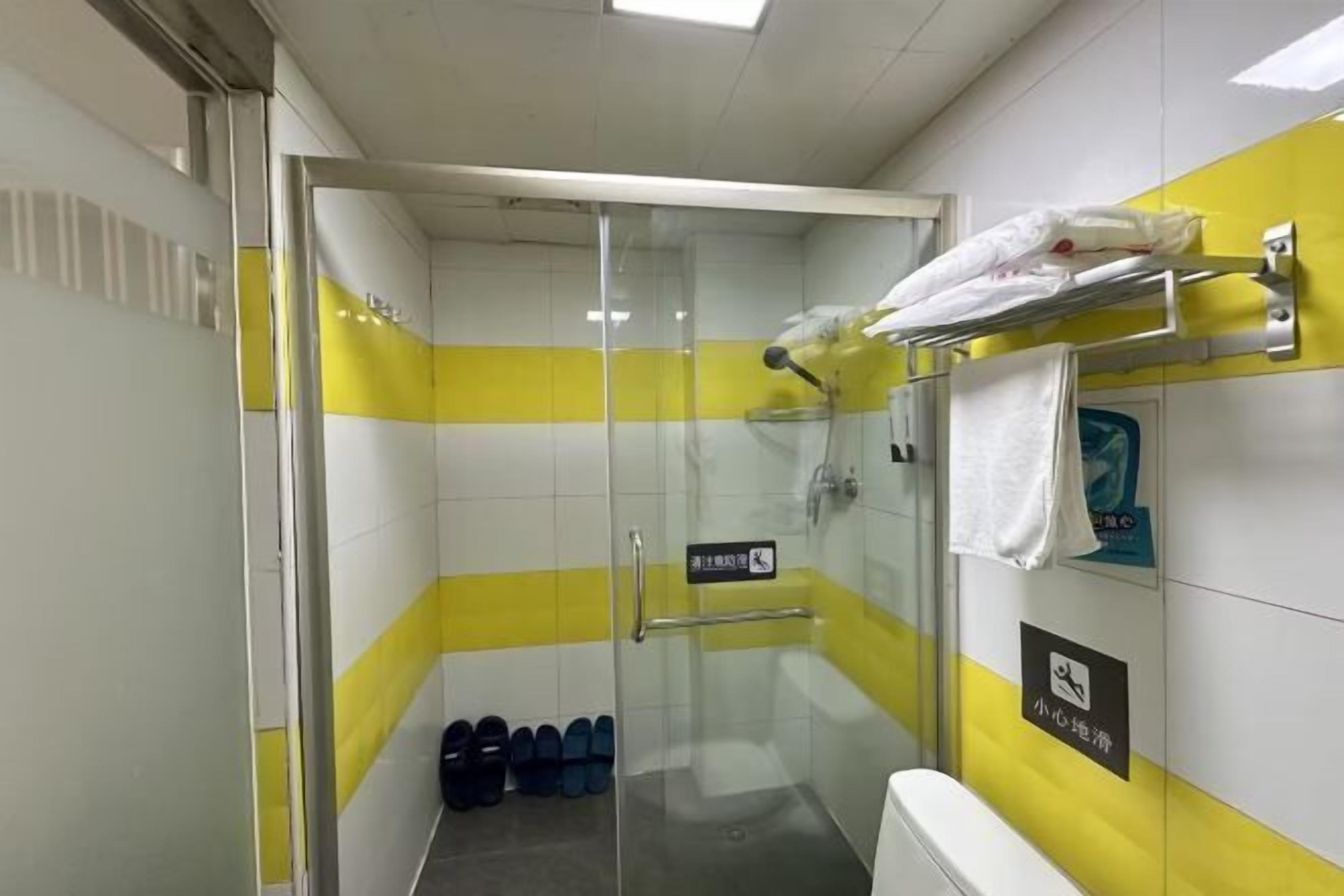 A bathroom with a glass shower enclosure, yellow and white walls, a towel rack, and a sign indicating a baby changing area.