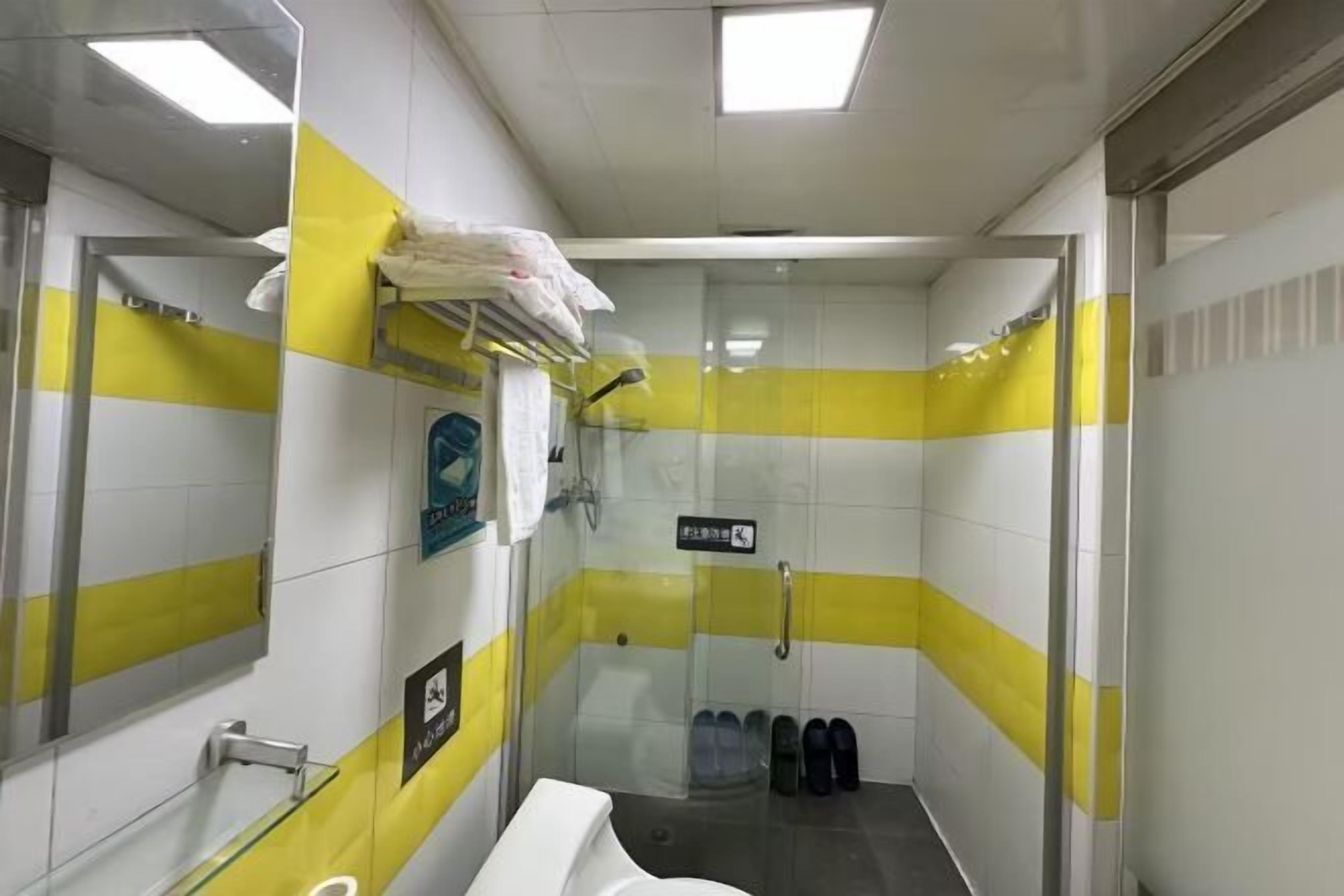 Et lille, smalt badeværelse med gul og hvide stribede vægge, en glasbrusekabine, en vask og et toilet.