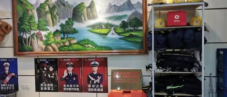 A room with a large landscape painting, a shelf with helmets, and a red suitcase.