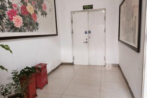 Un couloir avec une porte blanche, un tableau encadré accroché au mur et une plante en pot.