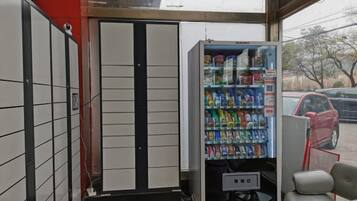 Una máquina expendedora con diversas bebidas y aperitivos, una puerta con un diseño en blanco y negro, y un coche aparcado fuera.