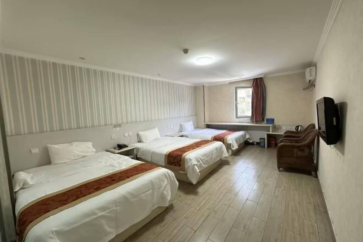A hotel room with three beds, a desk, a chair, and a television.