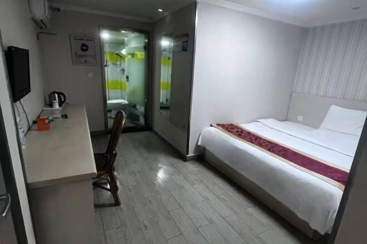 A hotel room with a bed, a desk, a chair, and a television.