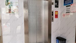En elevator med væg i marmor, en skraldespand og forskellige sikkerheds- samt informationsskilte.