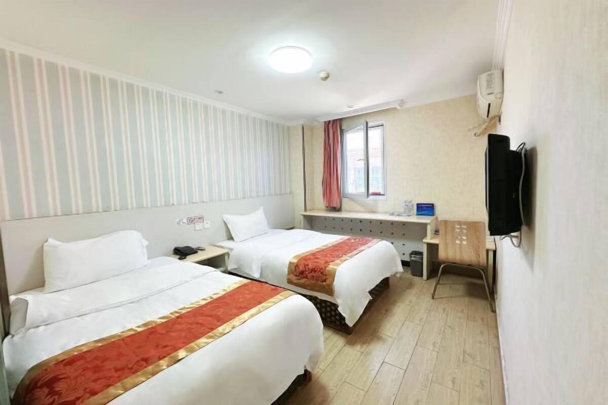 A hotel room with two beds, a desk, a chair, a TV, and a window.