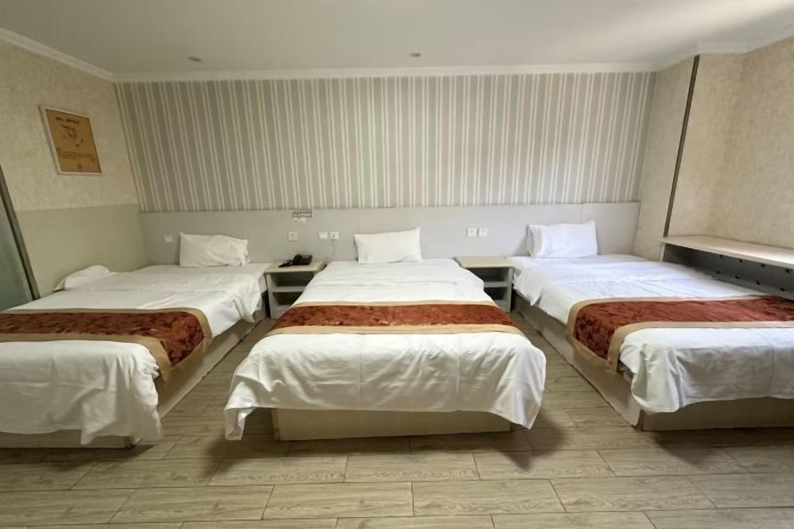 A hotel room with three single beds, a striped wall, and a wooden floor.