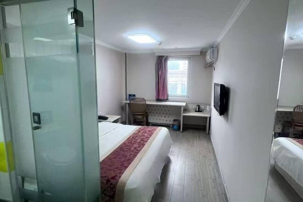 A hotel room with a bed, a desk, a chair, a TV, and a window with curtains.