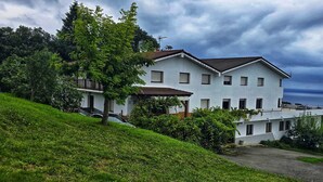 Un edificio de dos pisos con techo inclinado, rodeado de abundante vegetación y árboles.