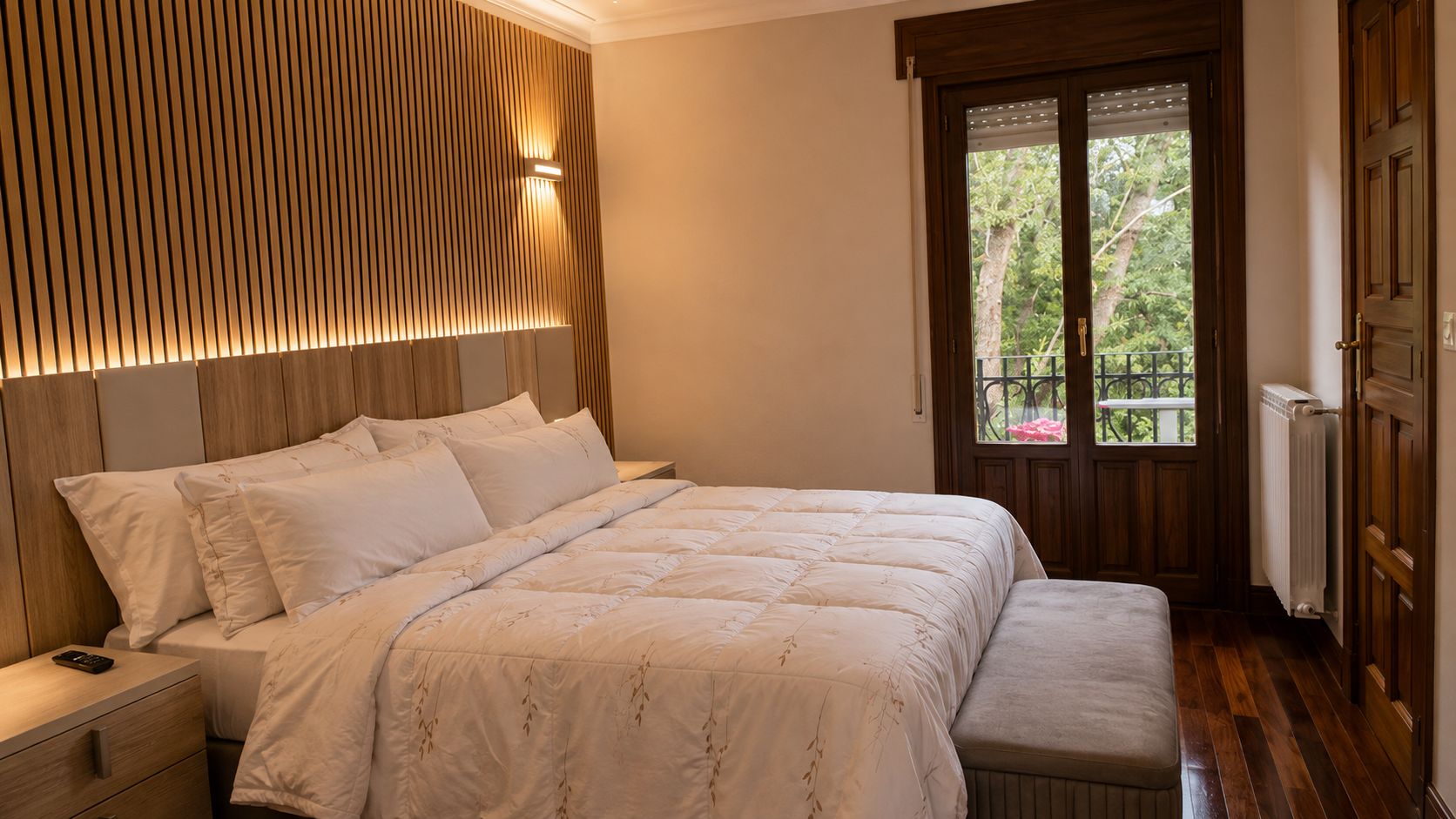 Un dormitorio con cama, mesitas de noche, ventana con vistas y cabecero de madera.