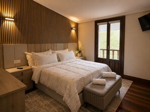 A bedroom with a large bed, bedside tables, a bench, a TV, and a window with a view. - Matzuri Nekazal Turismoa (Mutriku)