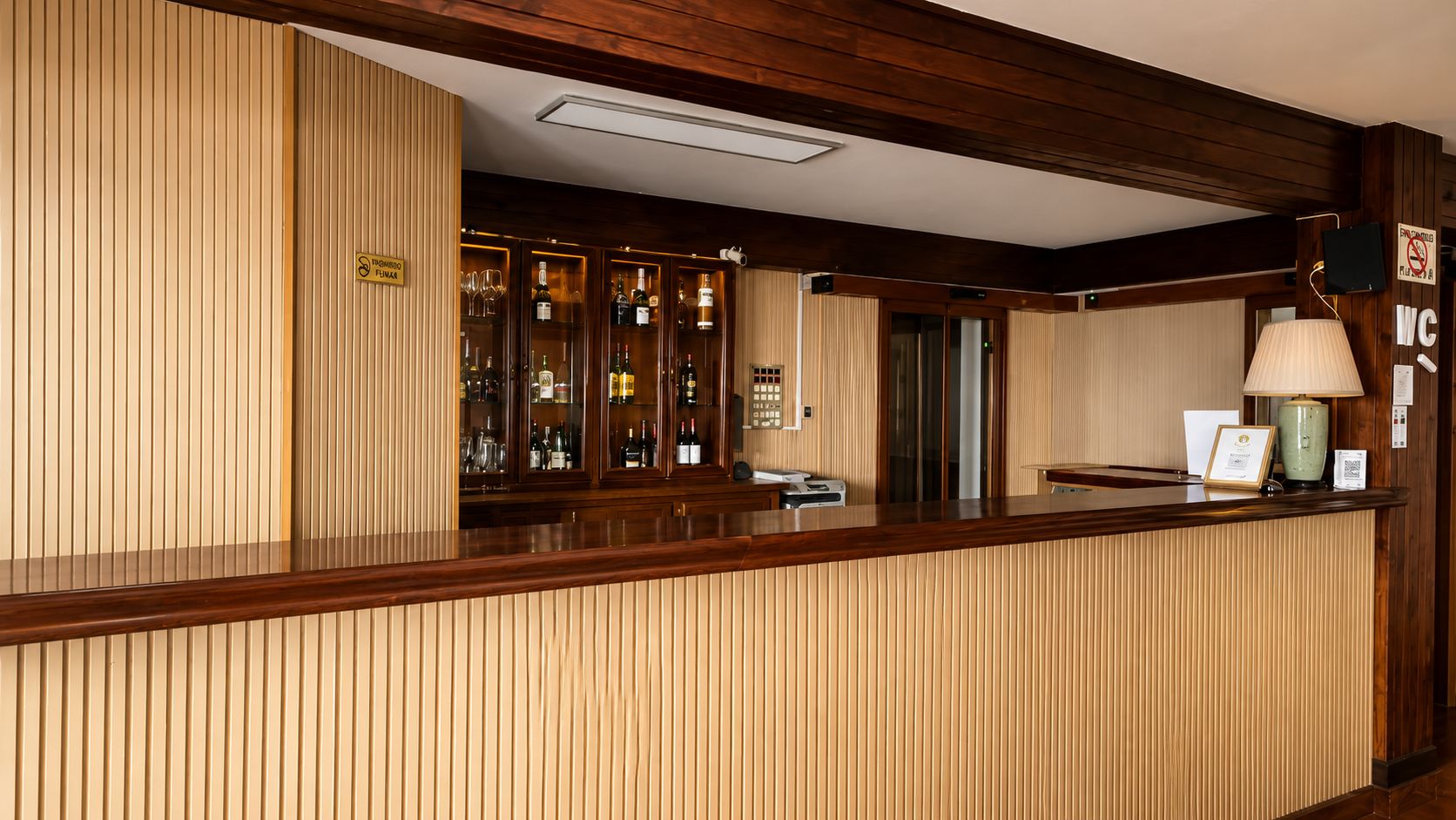 Un área de recepción con un mostrador de madera, una vitrina con botellas y un cartel que indica una zona para fumadores.