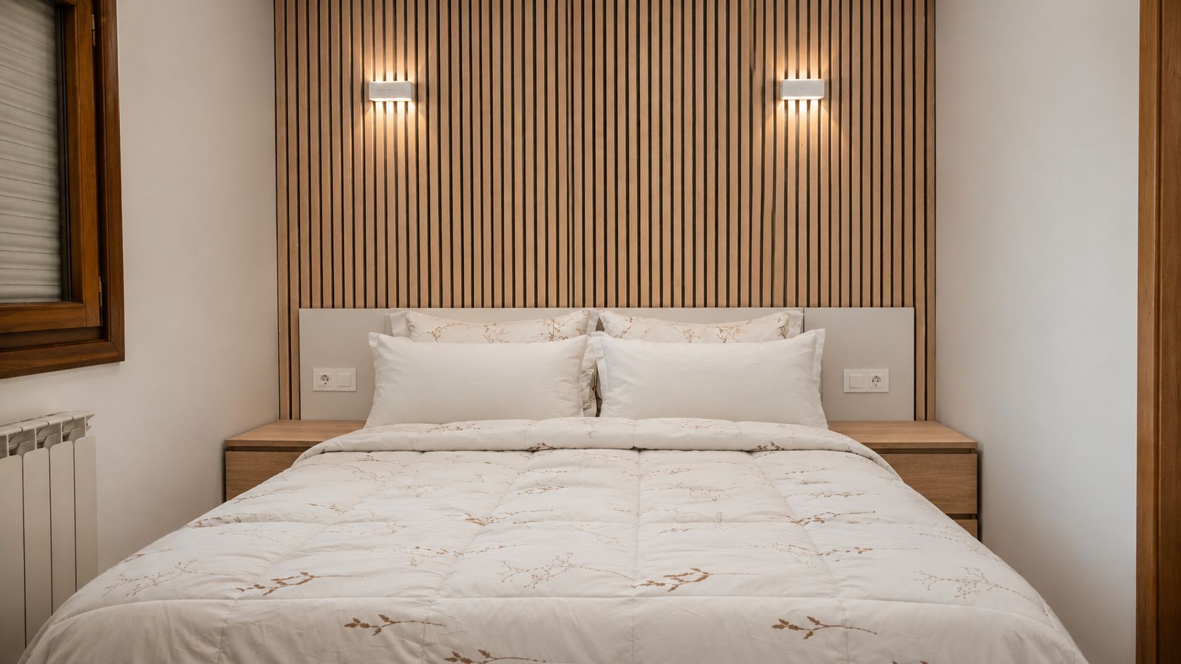 A bedroom with a bed, nightstands, a wooden slat wall, and two wall-mounted lights.