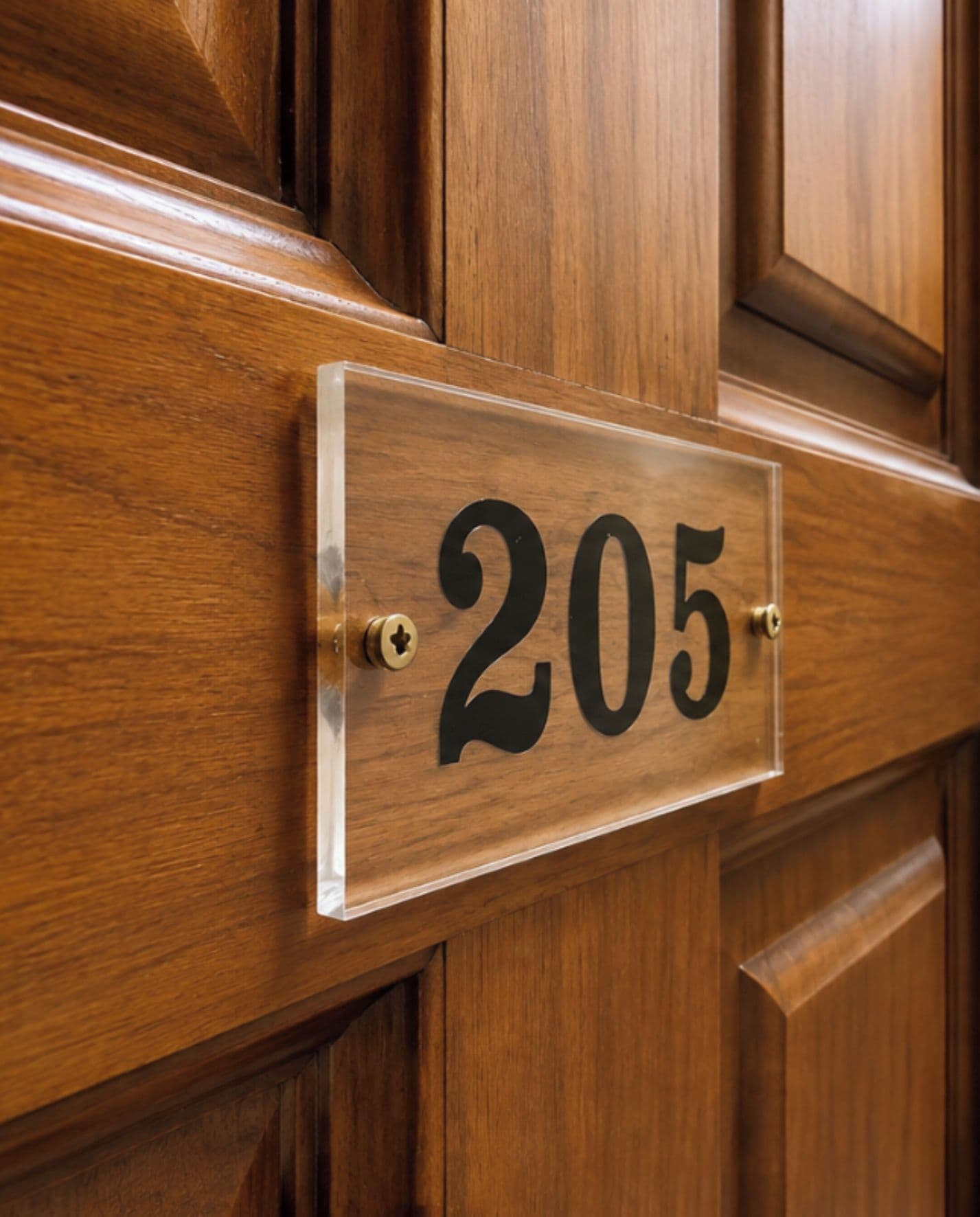 A wooden door with a clear, rectangular sign displaying the number 205.