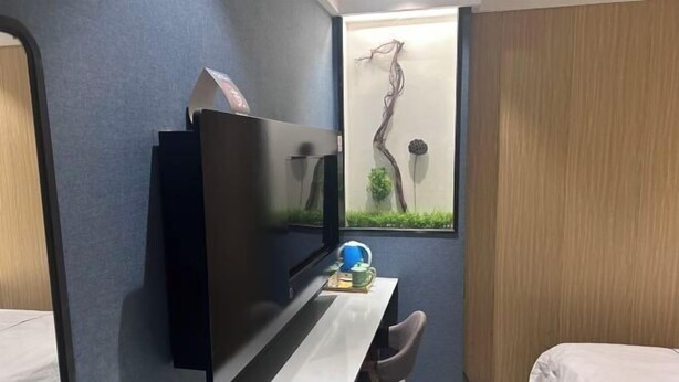 A hotel room with a bed, a desk with a flat-screen TV, a small table with a lamp, and a wall-mounted artwork. - Enjoy Hotel (Wuzhong Road) (Shanghai)