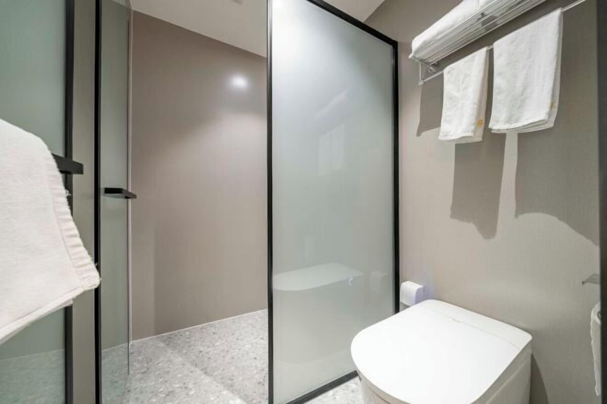 A modern bathroom with a glass shower enclosure, a white sink, and two towels hanging on the wall.