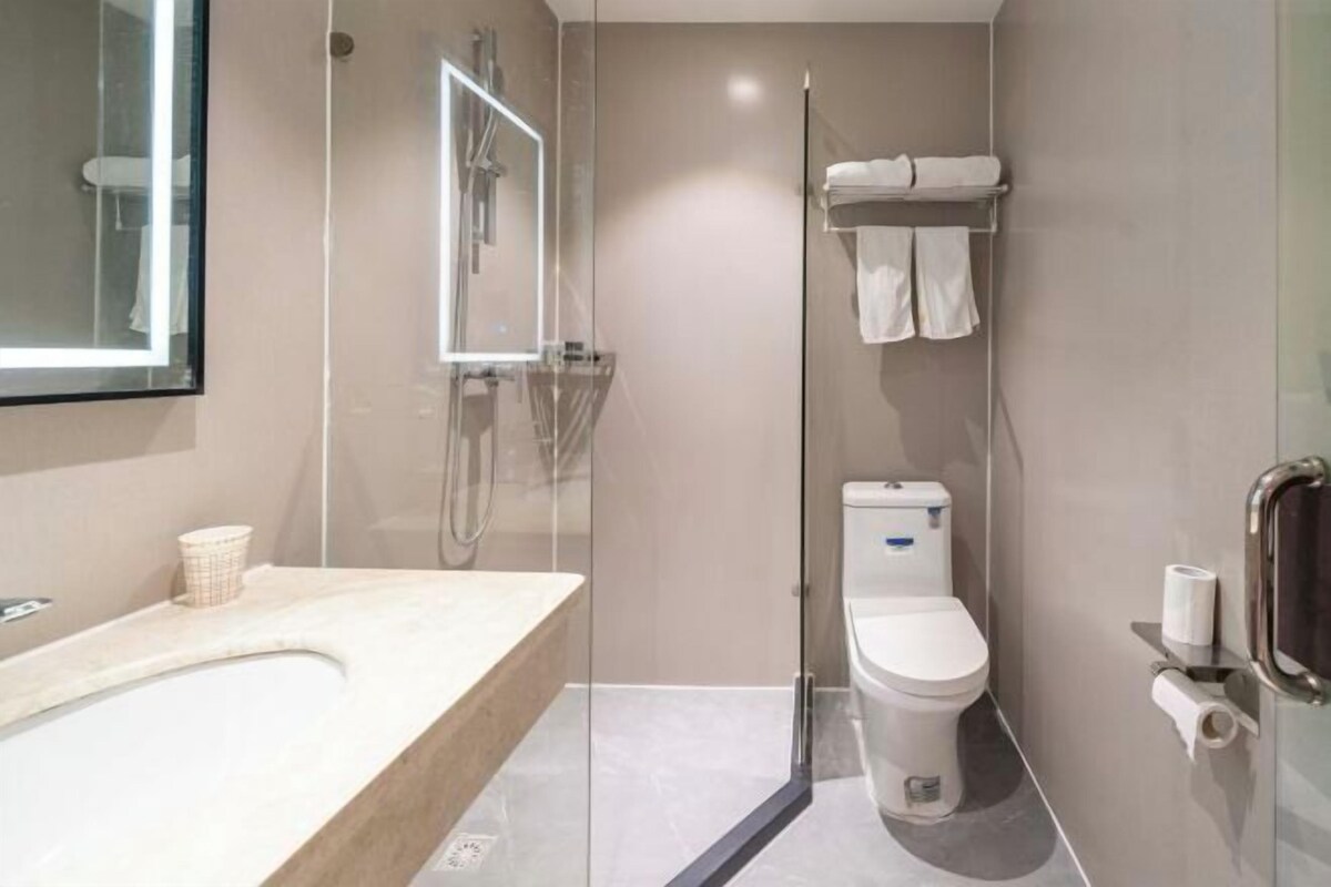 A modern bathroom with a glass shower enclosure, a toilet, and a sink with a mirror above it.