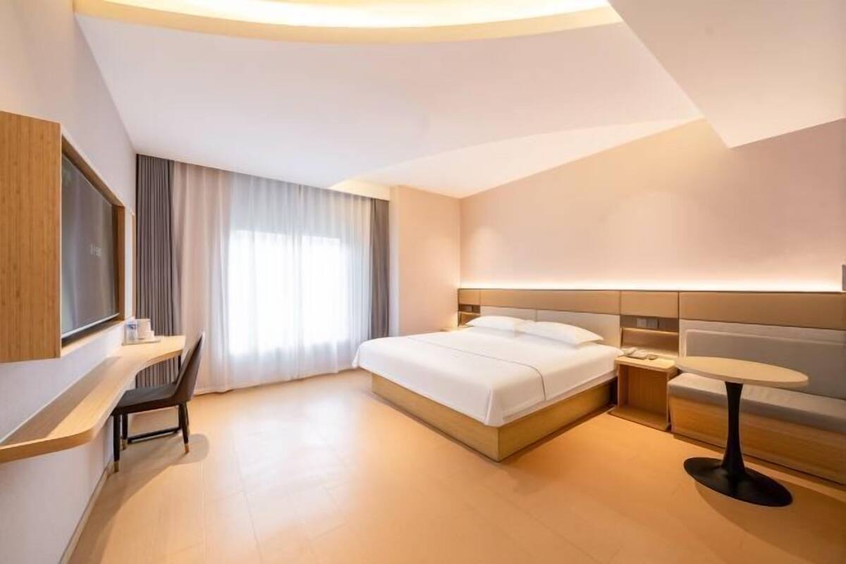 A modern hotel room with a bed, bedside table, chair, and a small round table.