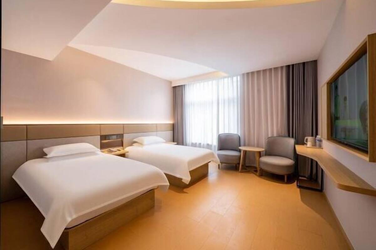A hotel room with two beds, a small table, a chair, and a TV.