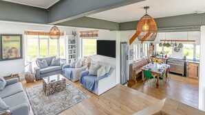 A spacious living area with a sofa set, a dining table, and a kitchen with wooden flooring.